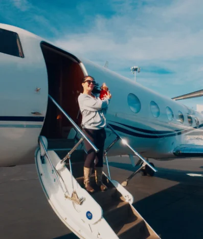 Person holding a small dog on private jet steps