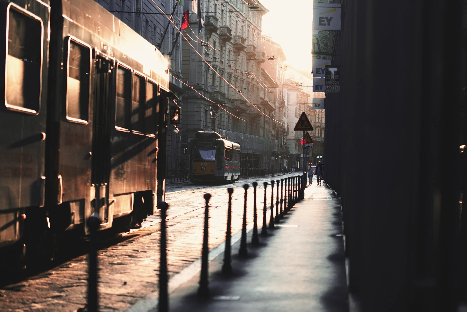 tram-9840971_1920 Sunlit tram line through a Milan street, long shadows and a few people walking.